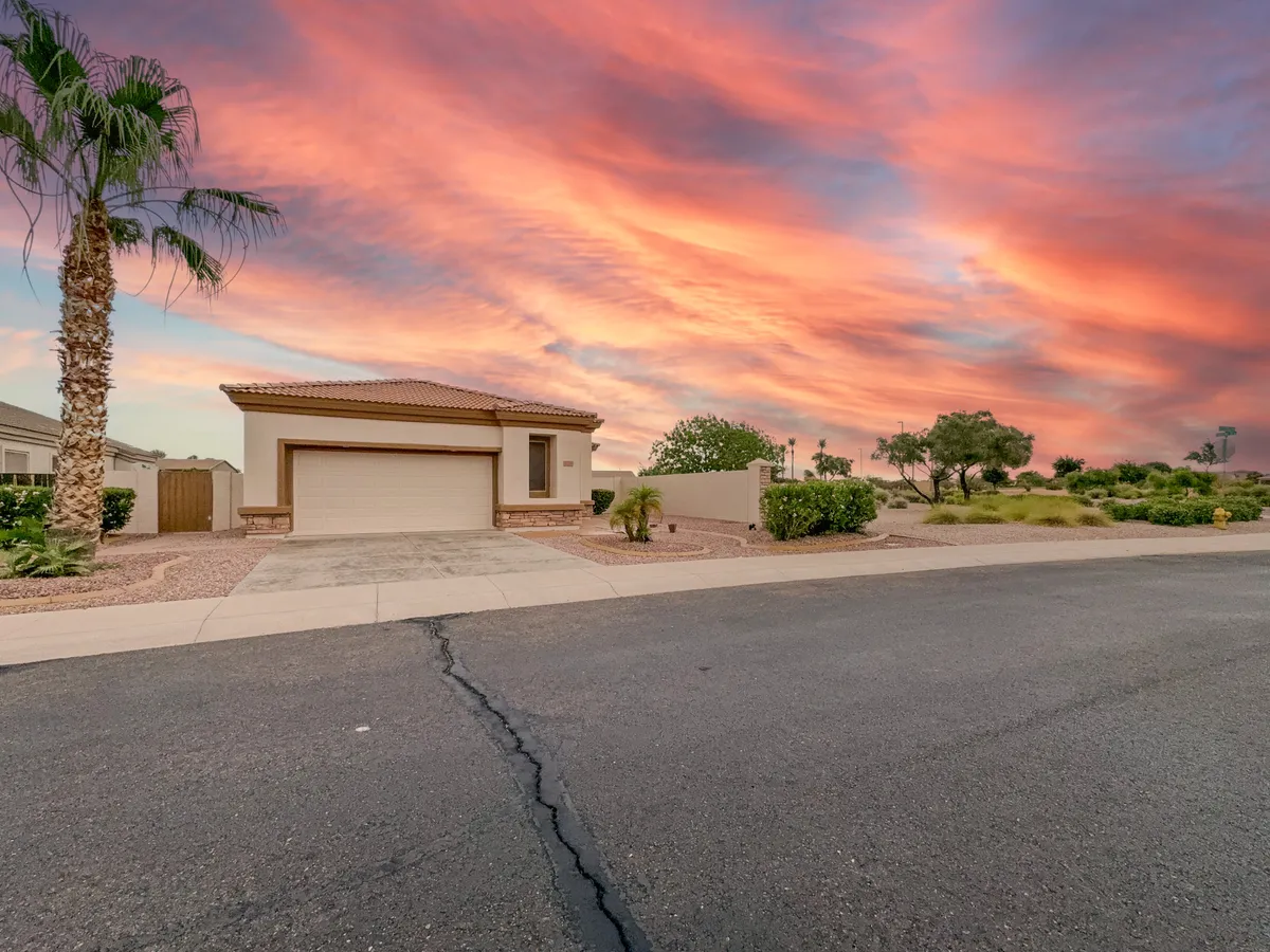 A picturesque exterior shot of a house framed by palm trees beneath a softly glowing sunset sky. The scene conveys a sense of tranquility, space, and the welcoming nature of the Seville community, with hints of garden and gathering areas that invite outdoor play or relaxation.