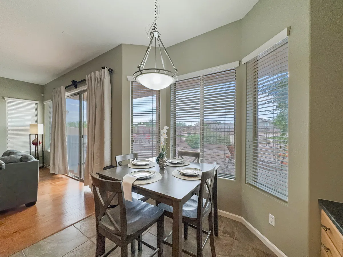 This image presents a bright dining table set near large windows, offering views outside and suggesting a connection to the backyard or patio. The natural light and warm setting evoke a sense of gathering after outdoor activities, like golf or grilling.