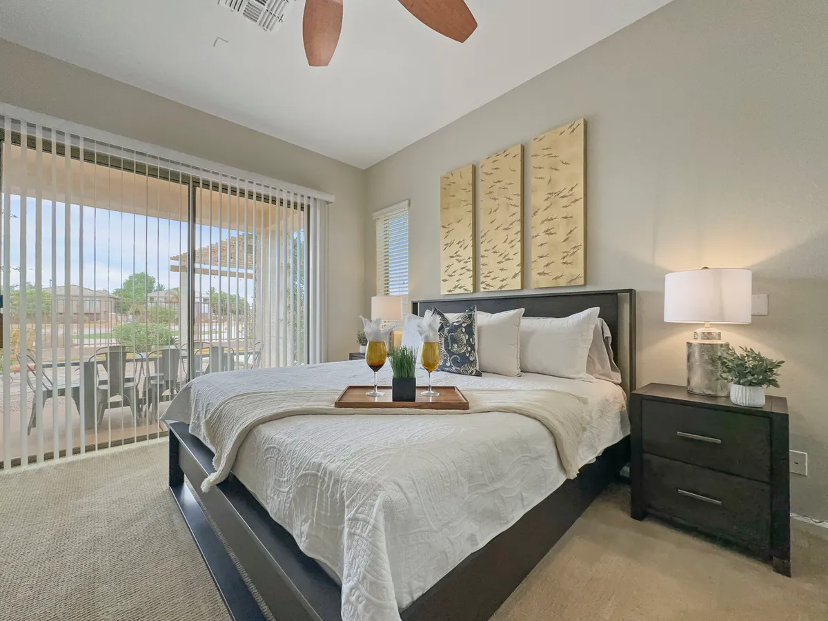 A serene bedroom with a plush bed adorned with decorative pillows, a nightstand with a modern lamp, and a sliding glass door leading directly to a patio. Soft natural light fills the room, creating a tranquil ambiance ideal for both restful sleep and peaceful mornings.