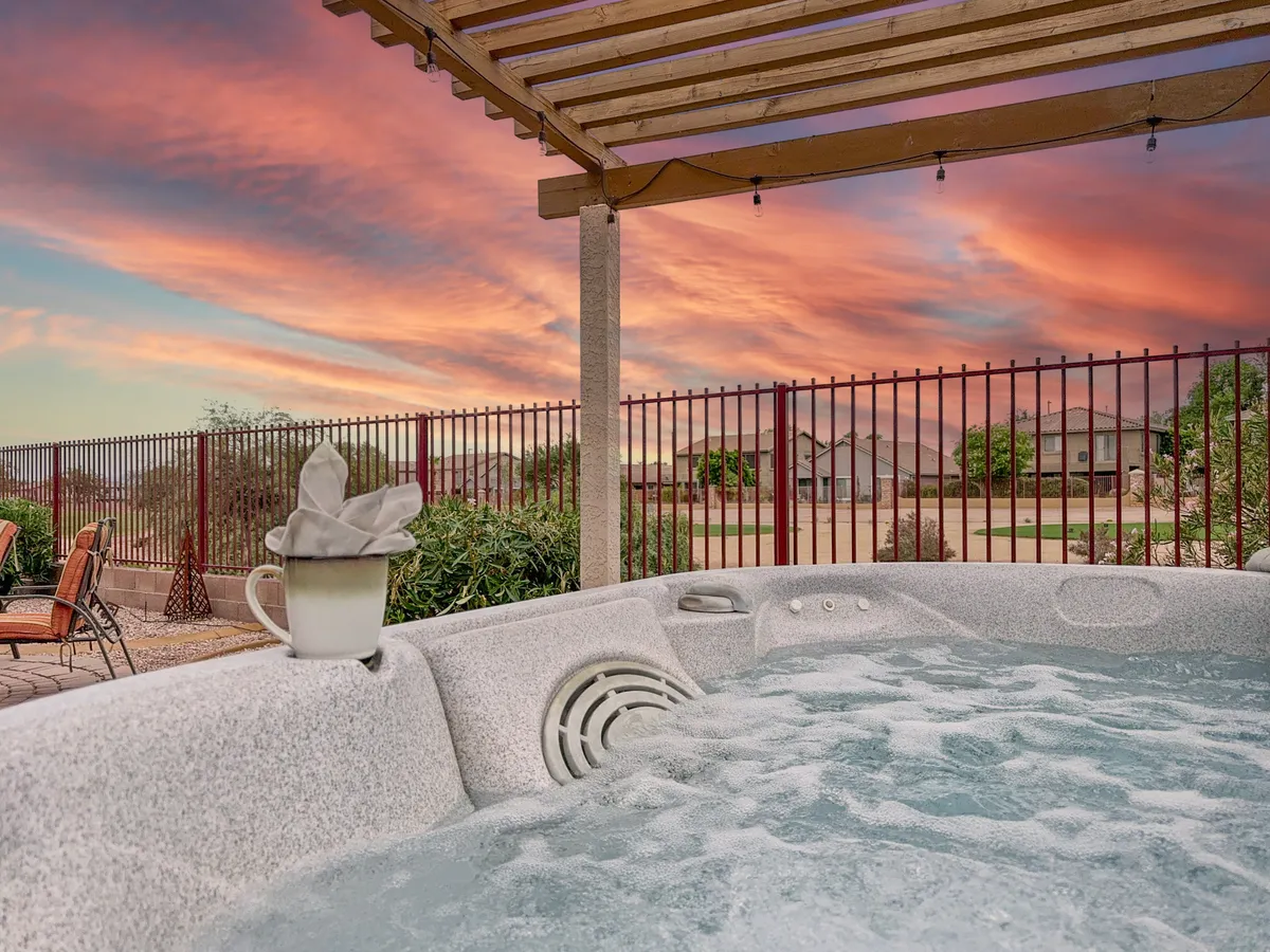 An inviting exterior scene featuring a private hot tub set against a glowing sunset sky. A coffee cup suggests a relaxing moment, while the surrounding landscape hints at spaciousness and tranquility.