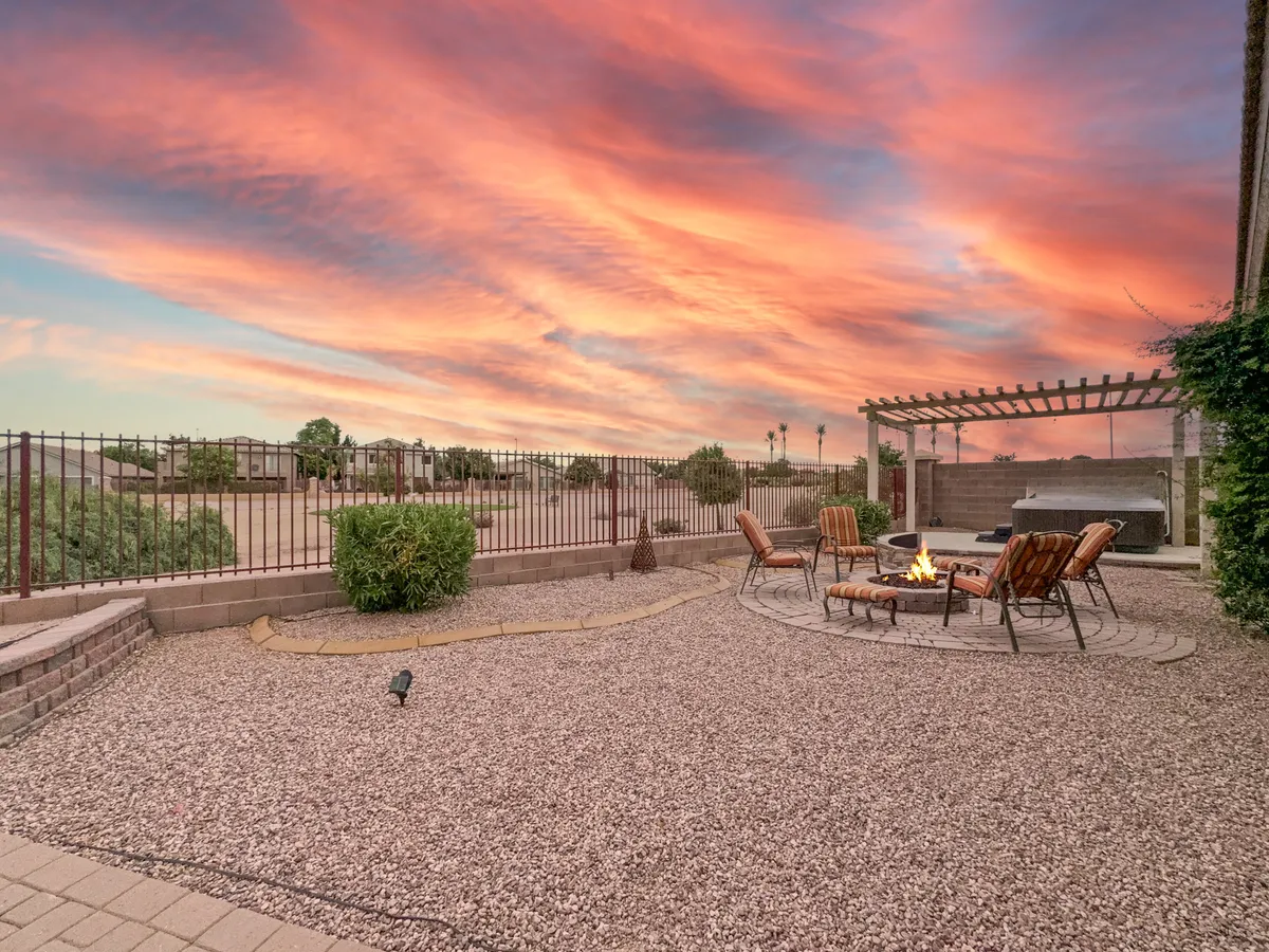 A cozy exterior seating area with a fire pit, surrounded by comfortable chairs and set against a vibrant sunset sky. The ambient lighting and comfortable setup suggest a perfect space for gathering after work or enjoying relaxed evenings outdoors.
