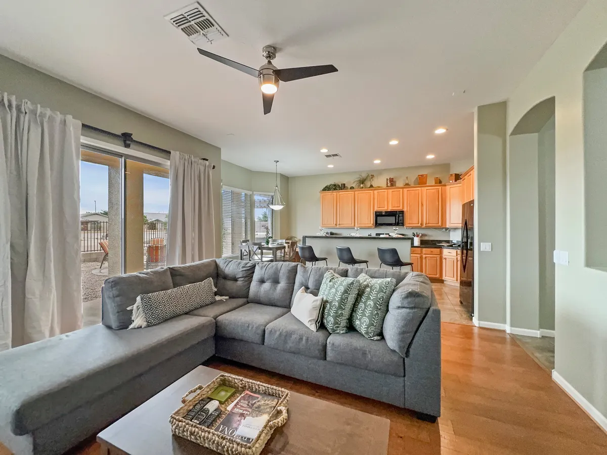 A spacious open-concept living area featuring a large sectional sofa, a kitchen island with bar stools, and a dining area by the window. Natural light fills the space, and the layout seamlessly connects living, dining, and kitchen zones, making it ideal for gatherings and family time.