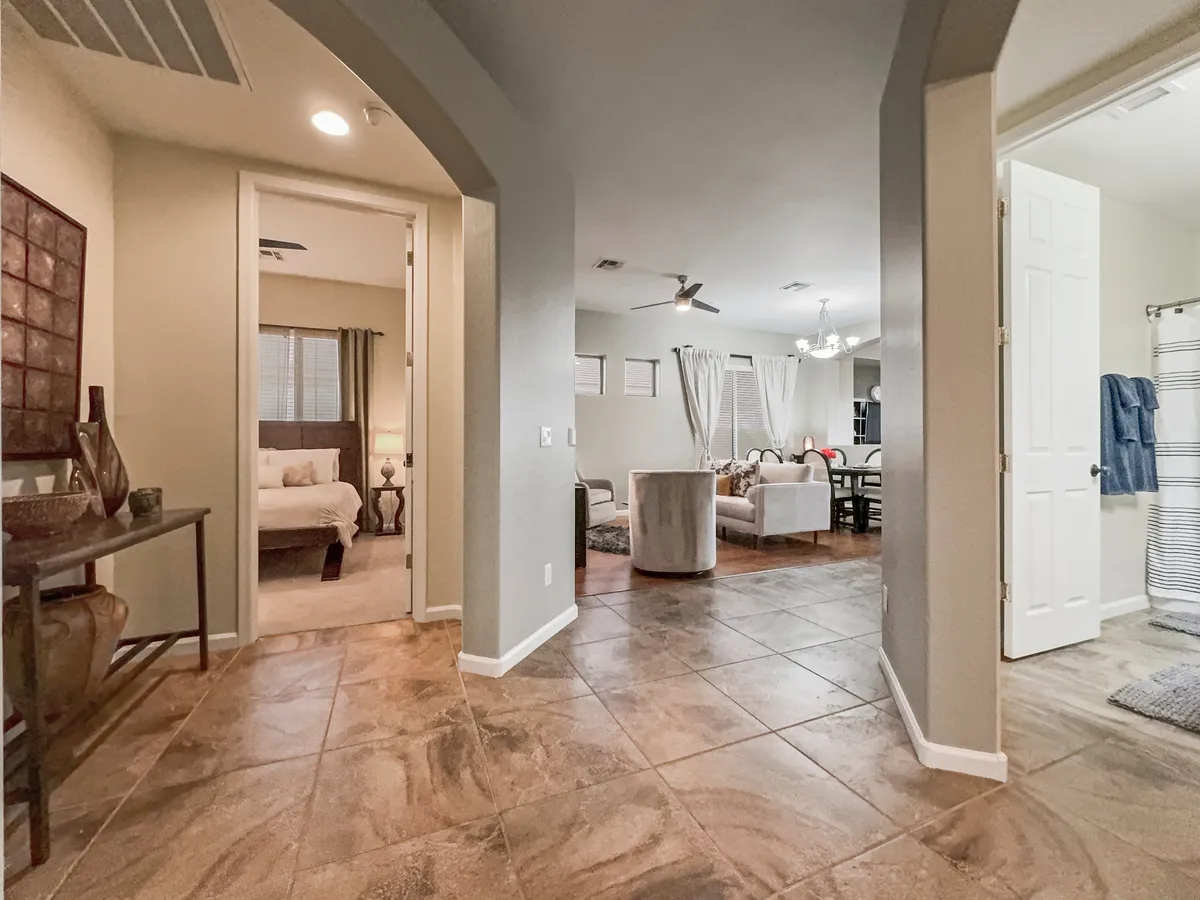 This image features an inviting view from the entrance hallway, revealing a glimpse of the living room furniture, dining area, and a doorway leading to the bedroom. The layout subtly connects interior gathering spaces to the rest of the home, and hints at potential access to outdoor amenities through open sight lines.