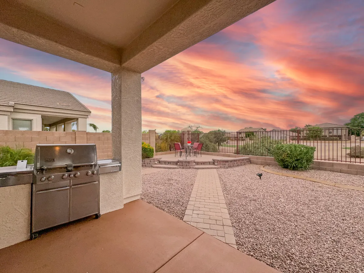 An outdoor kitchen area with a stainless steel grill and a cozy patio set, all backdropped by a stunning sunset sky. The setting is inviting for alfresco dining and entertaining guests, with comfortable seating close at hand.
