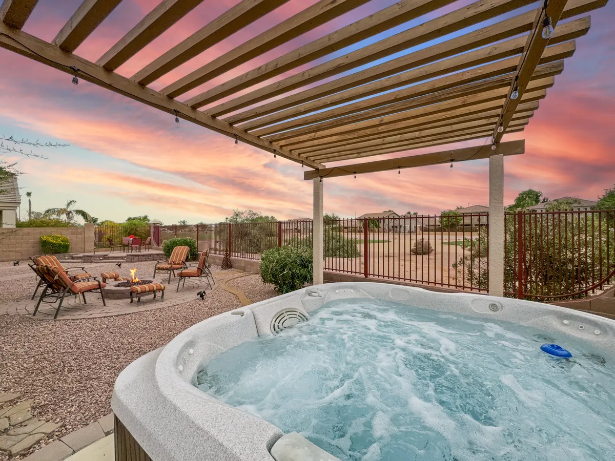 An inviting backyard scene featuring a hot tub and a fire pit surrounded by lounge chairs. The sky is awash in sunset hues, setting a tranquil and social atmosphere ideal for evening gatherings. The setup encourages relaxation and togetherness, perfect for families and friends.